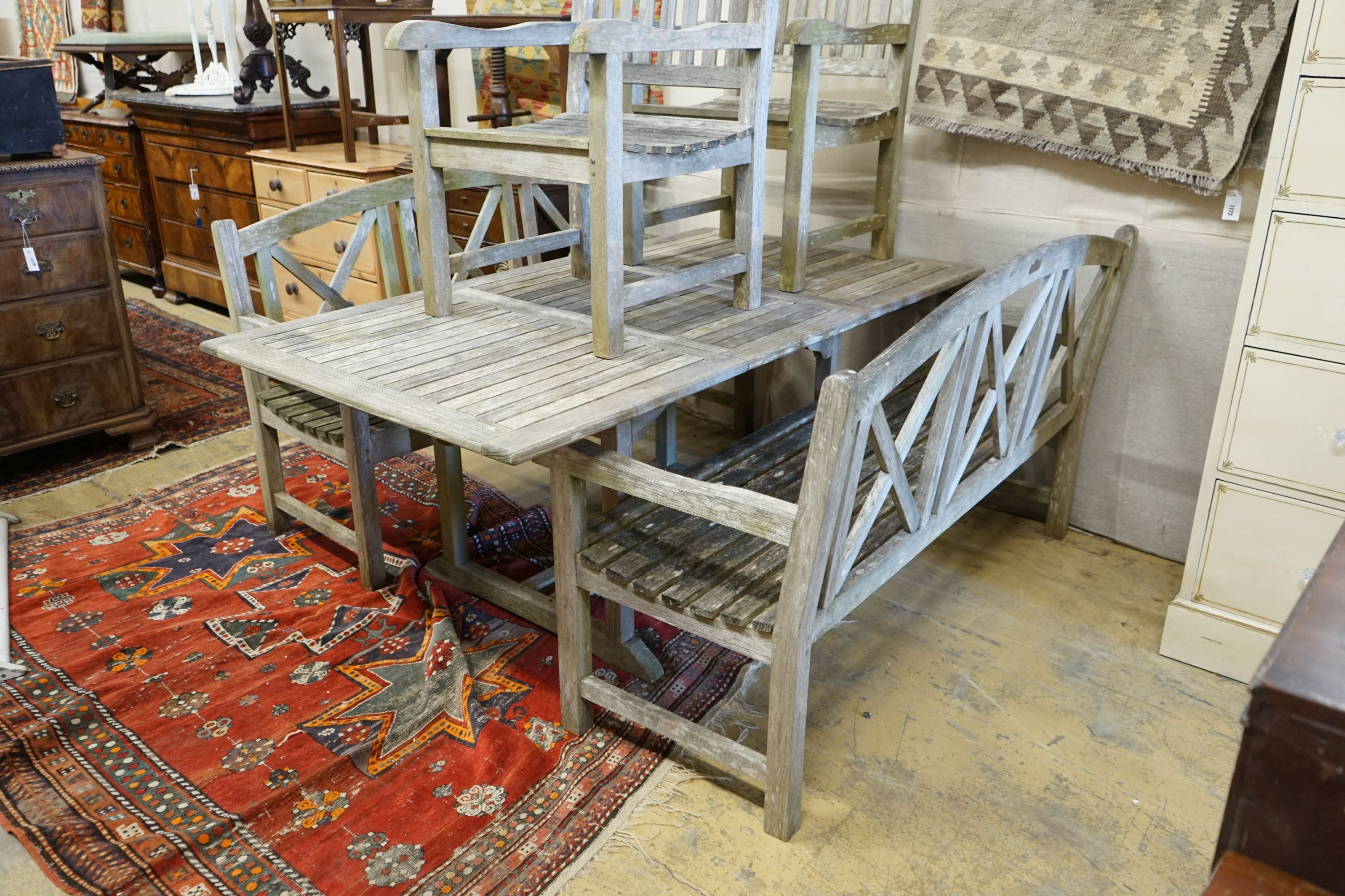 A rectangular weathered teak extending garden table, 180cm extended x 100cm x 74cm, together with a pair of weathered teak garden benches, width 153cm and a pair of teak elbow chairs